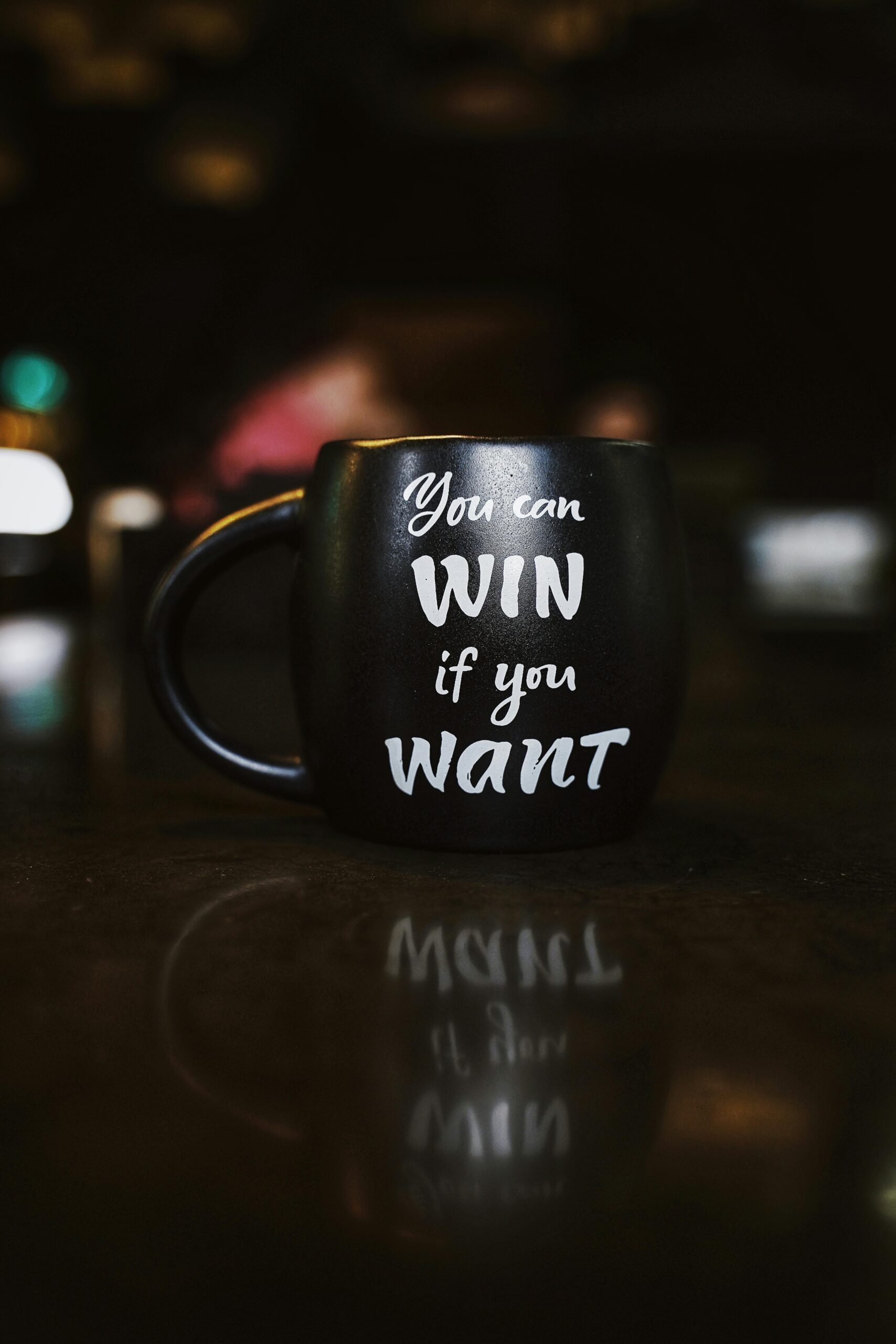 Black ceramic mug on a dark surface with white text that reads: “You can WIN if you WANT.” Motivational quote in a café-style setting, symbolising mindset and success.