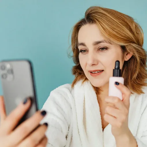 Woman creating social media content on smartphone while showcasing a skincare product, representing influencer marketing and brand promotion